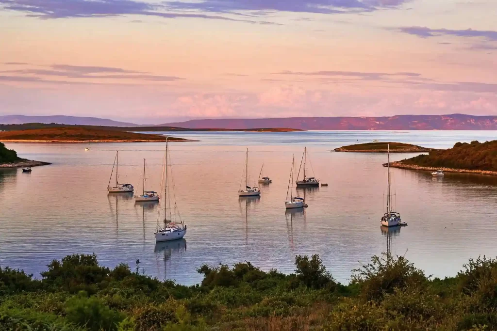 Sailboats anchored in a calm bay at sunset with small islands