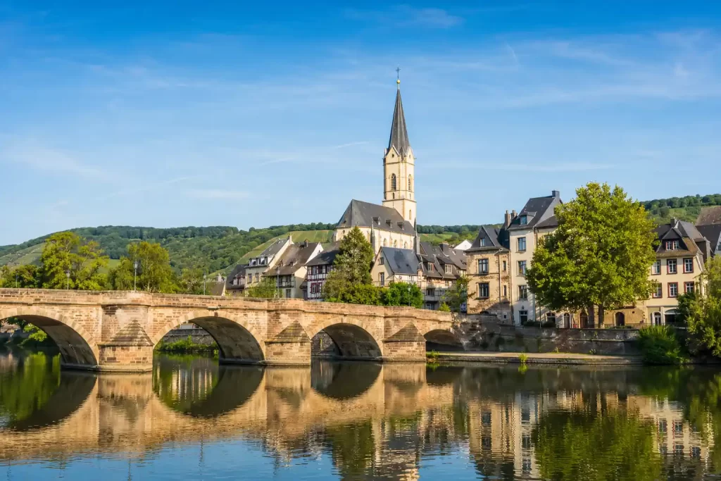 Scenic European riverside town with a stone bridge, historic buildings, and a church tower