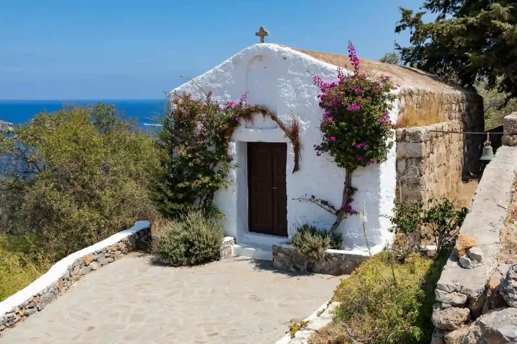 Whitewashed Greek chapel surrounded by bougainvillea overlooking the blue sea